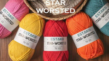 Five colourful Estako Star-Worsted skeins fanned around a basket, each ball band showing its label and dye-lot information.