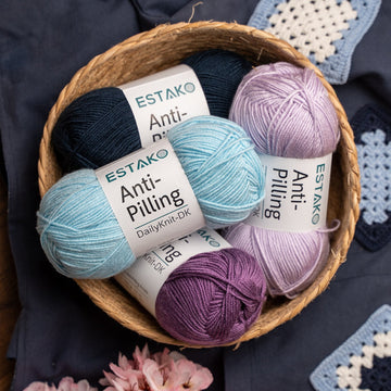 Colorful skeins of Estako DailyKnit-DK anti-pilling acrylic yarn in a basket beside a crocheted granny square.