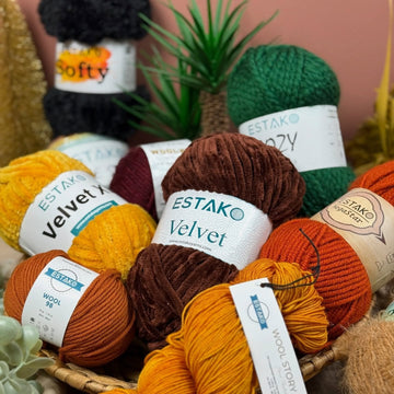 An assortment of Estako yarn skeins in cotton, wool blend, and acrylic, arranged by fiber on a wood table.
