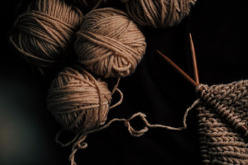 Flat lay of warm brown yarn balls beside wooden knitting needles, ready for a new project