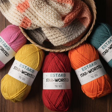 Skeins of Estako Star-Worsted wool blend yarn in autumn shades, stacked for a fall scarf project.