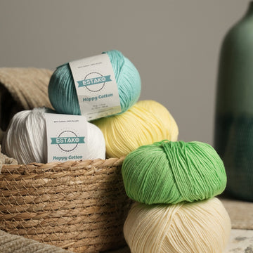 Estako Happy Cotton yarn balls in teal, cream, yellow, and green in a woven basket