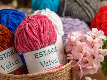 A basket of colourful Estako yarn in pink, blue, red and lavender with flowers, the multi-colour palette granny-square blankets are built from.