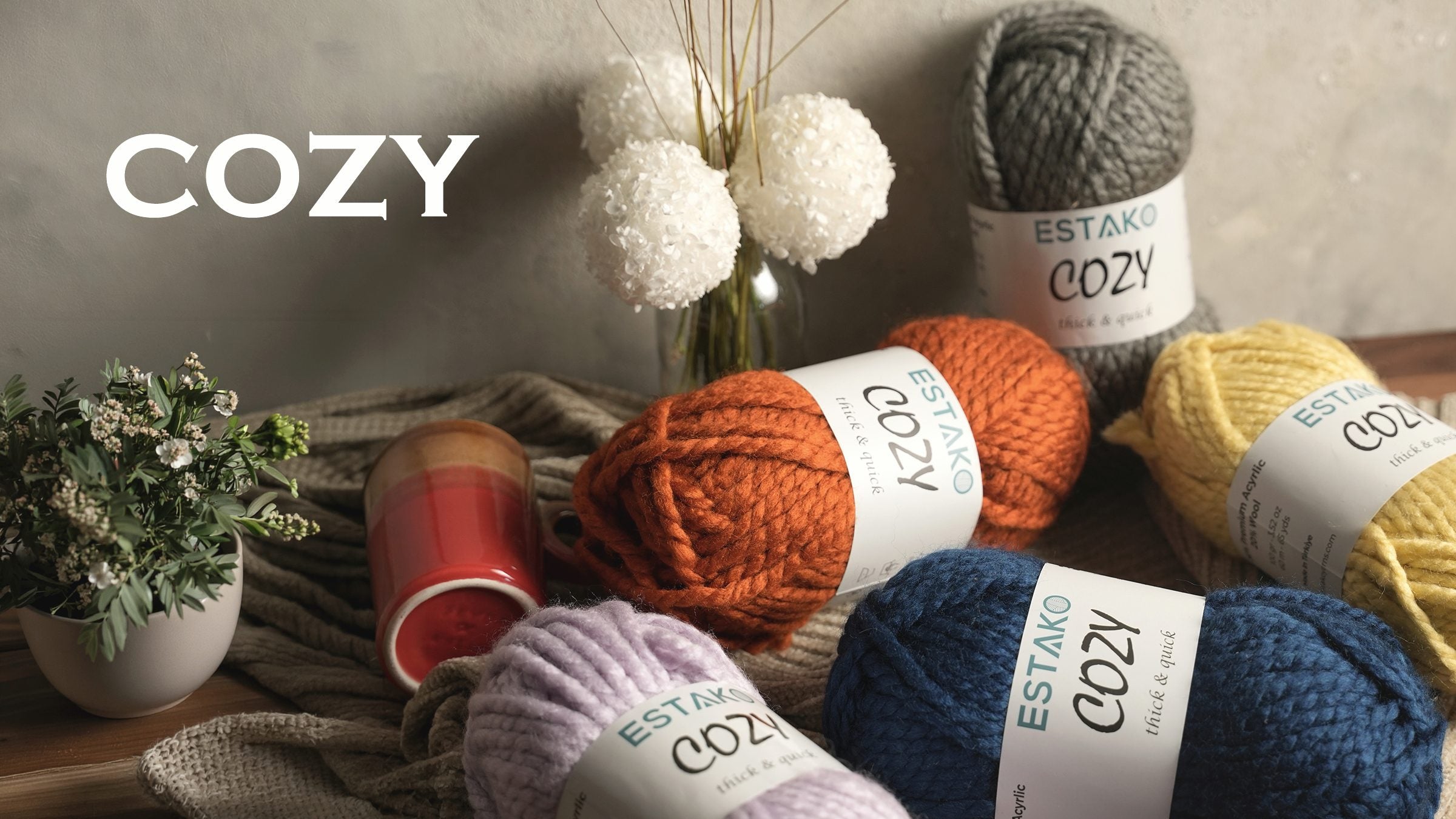 Estako Cozy super-bulky yarn skeins in orange, lilac, blue and yellow with a knitted throw.