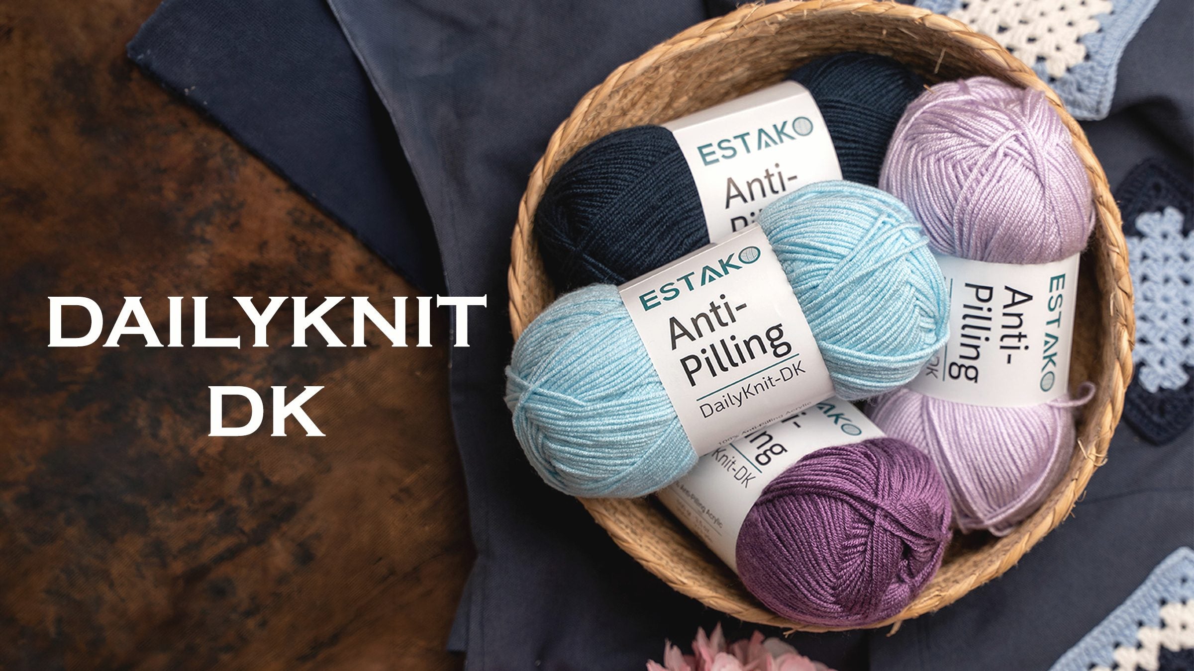 A basket of Estako DailyKnit-DK yarn in navy, blue, lilac and plum next to a crocheted granny square.